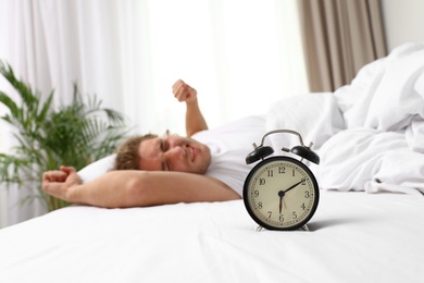Alarm clock and blurred sleepy man on background, space for text. Bedtime