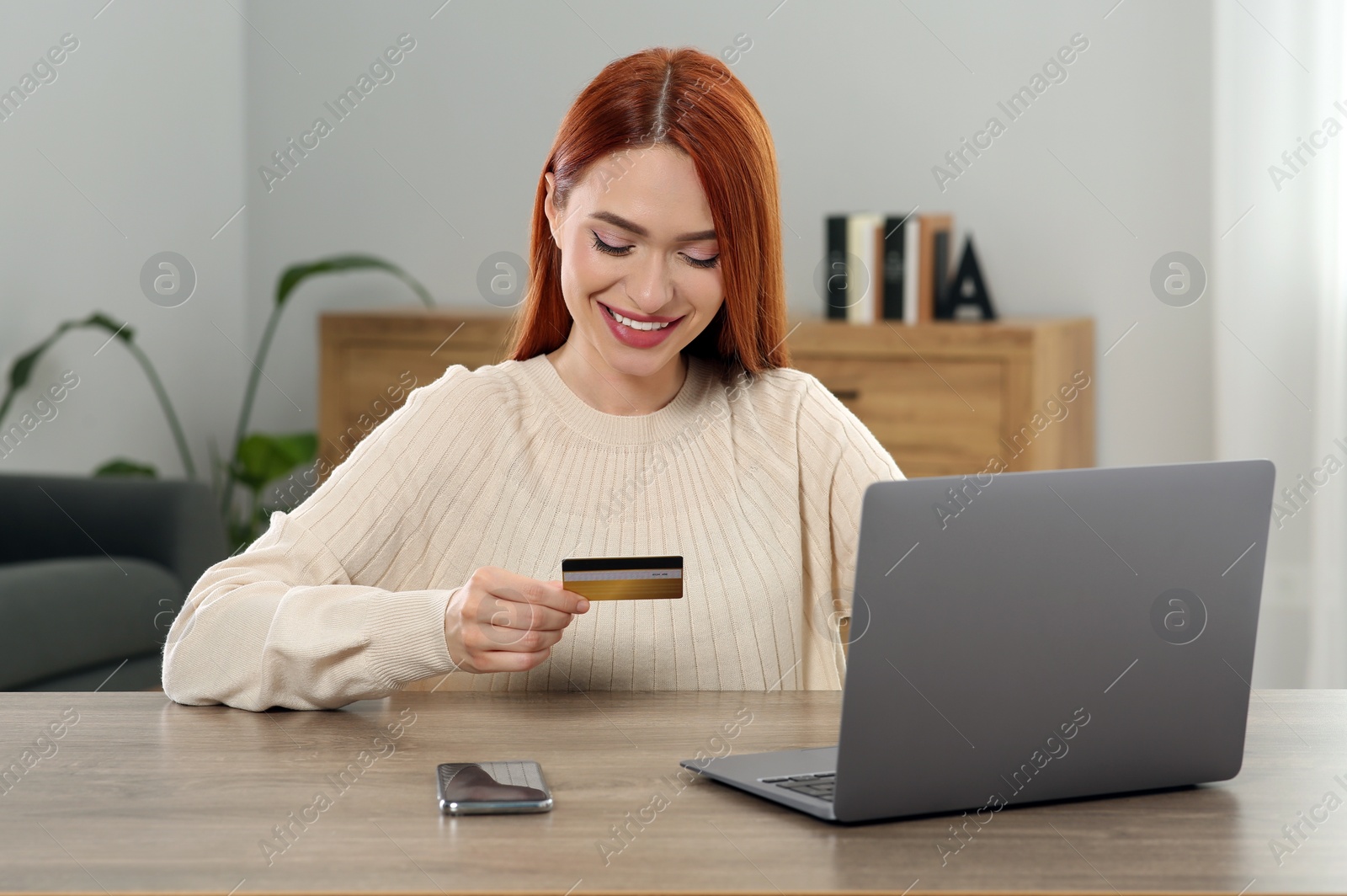 Photo of Happy woman with credit card using laptop for online shopping at wooden table in room