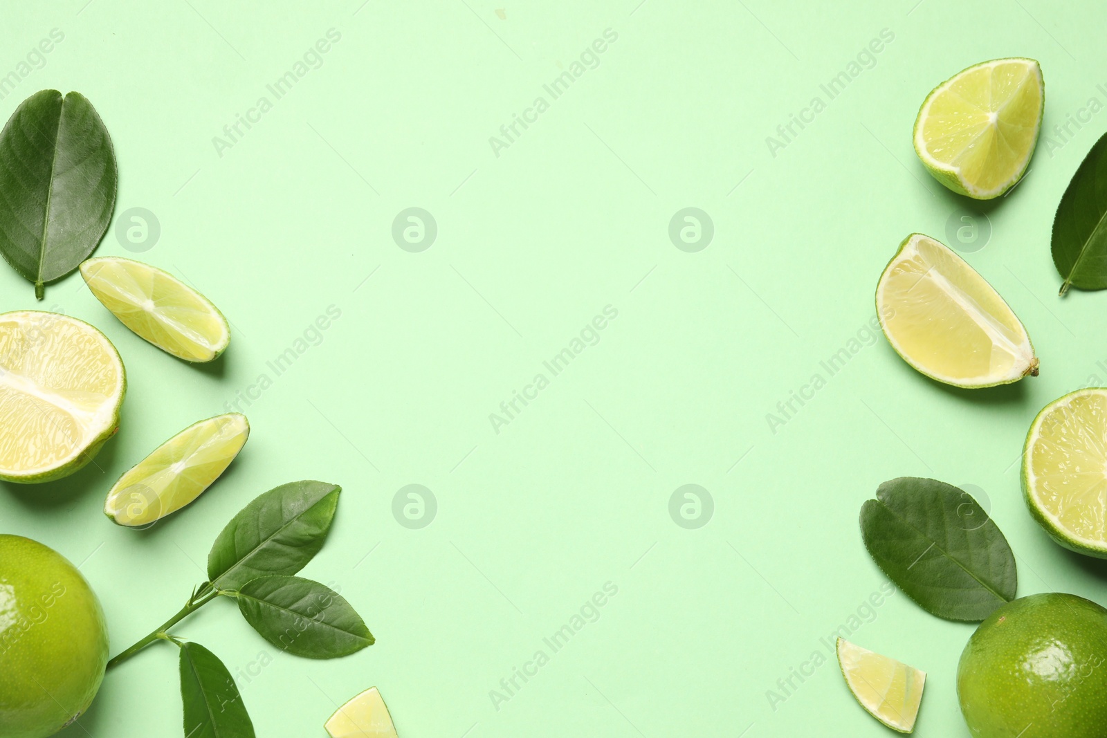 Photo of Whole and cut fresh ripe limes with leaves on light green background, flat lay