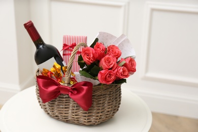 Photo of Wicker basket with gift, bouquet and wine on white table indoors