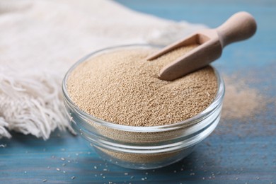 Photo of Bowl and scoop with active dry yeast on light blue wooden table, closeup