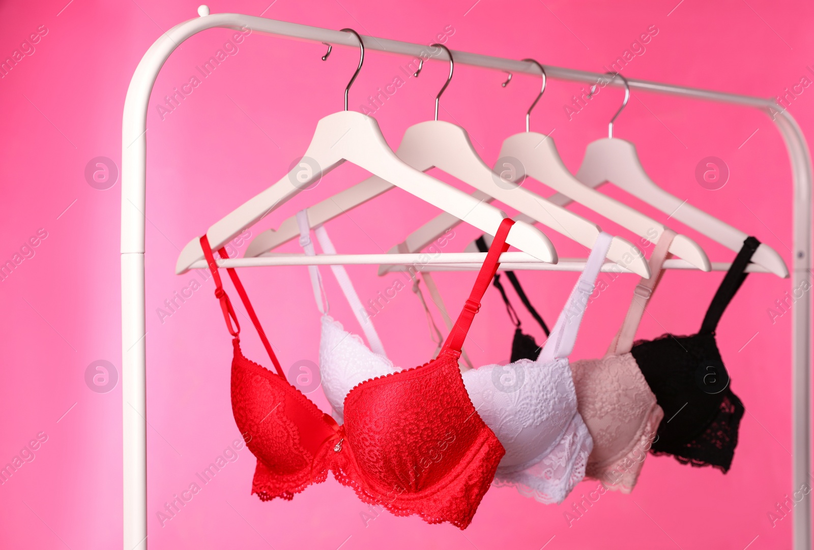 Photo of Hangers with beautiful lace bras on rack against pink background. Stylish underwear