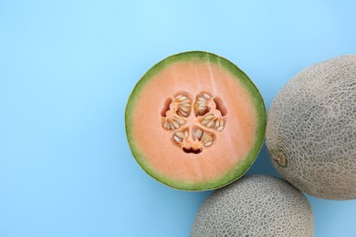 Photo of Whole and cut fresh ripe cantaloupe melons on light blue background, flat lay. Space for text