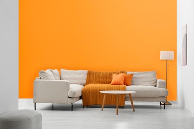 Photo of Stylish sofa and coffee table in room with orange walls. Interior design