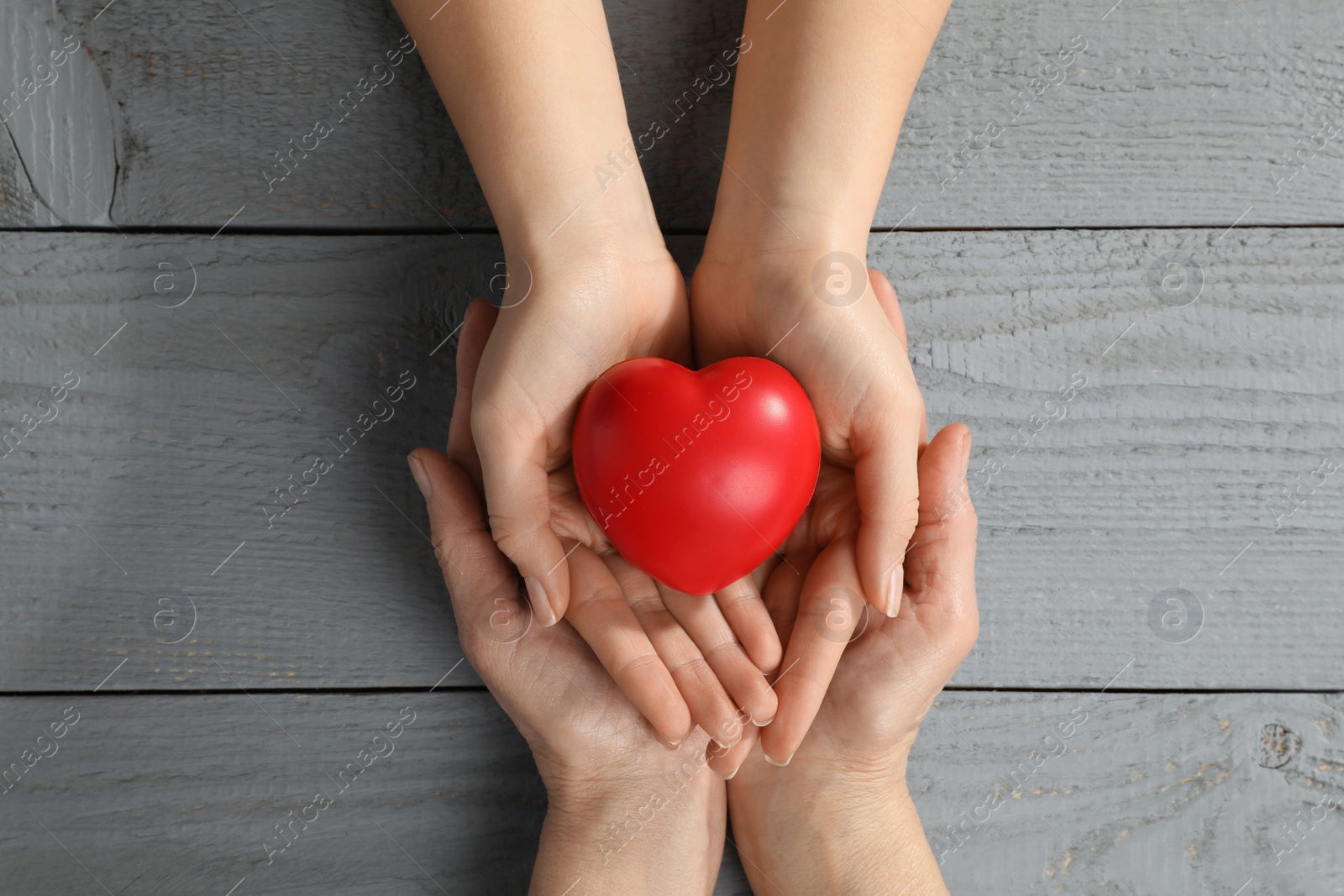 Photo of Young and elderly women holding red heart at grey wooden table, top view