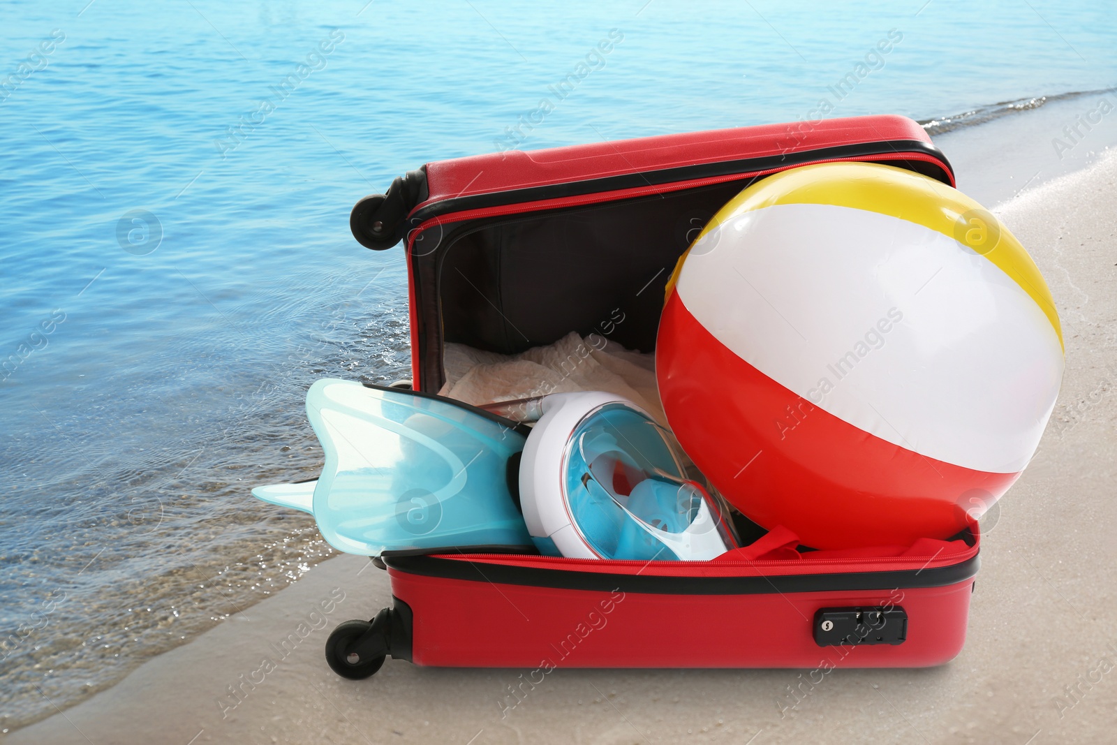 Image of Suitcase with different beach objects on sand near sea