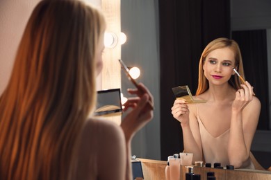 Beautiful woman applying makeup near mirror in room