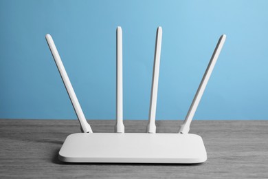 Photo of New white Wi-Fi router on wooden table against light blue background