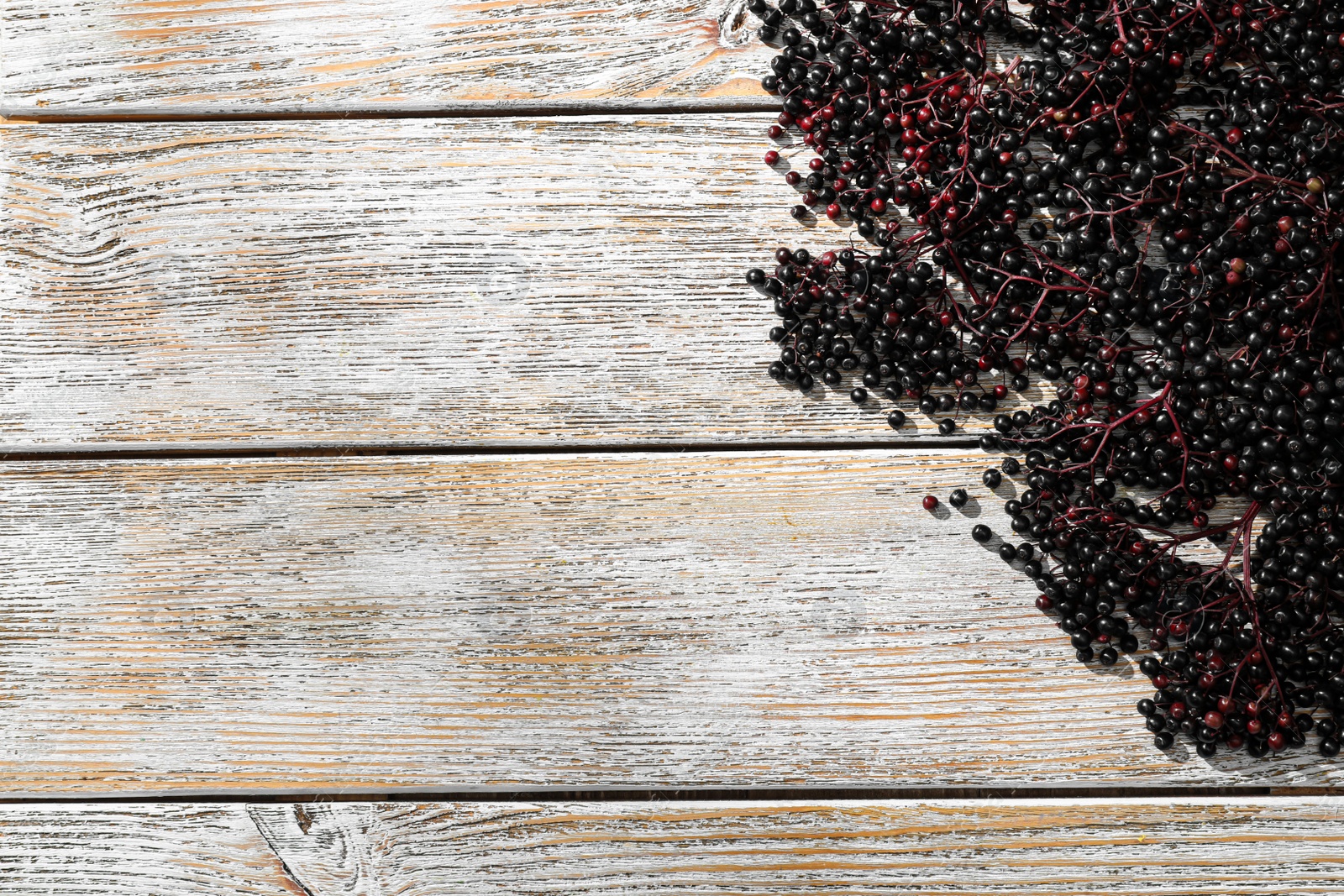 Photo of Black elderberries (Sambucus) on old wooden table, flat lay. Space for text