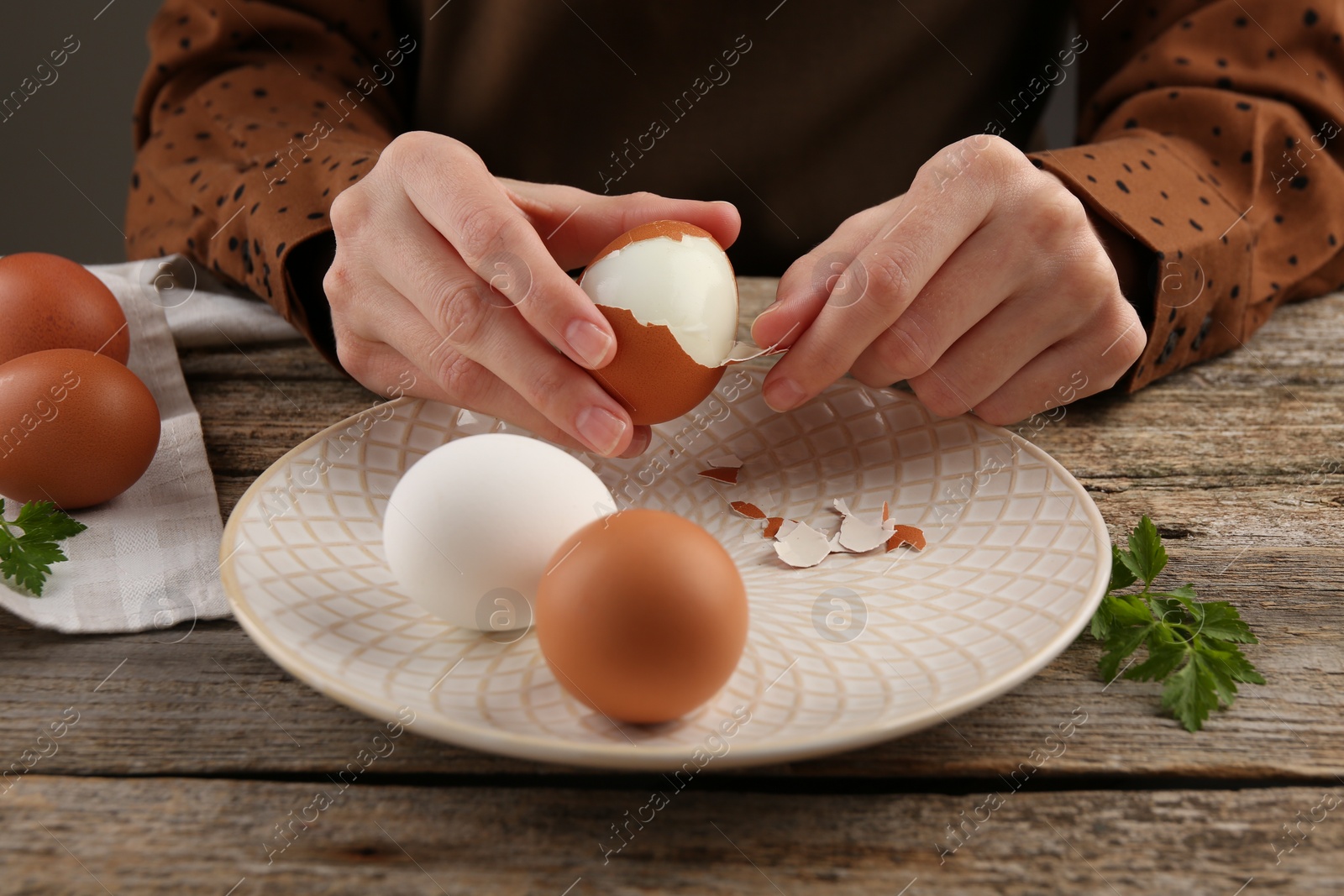 Photo of Woman peeling boiled egg at old wooden table, closeup