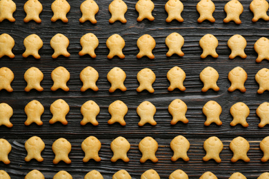 Photo of Delicious goldfish crackers on black wooden table, flat lay