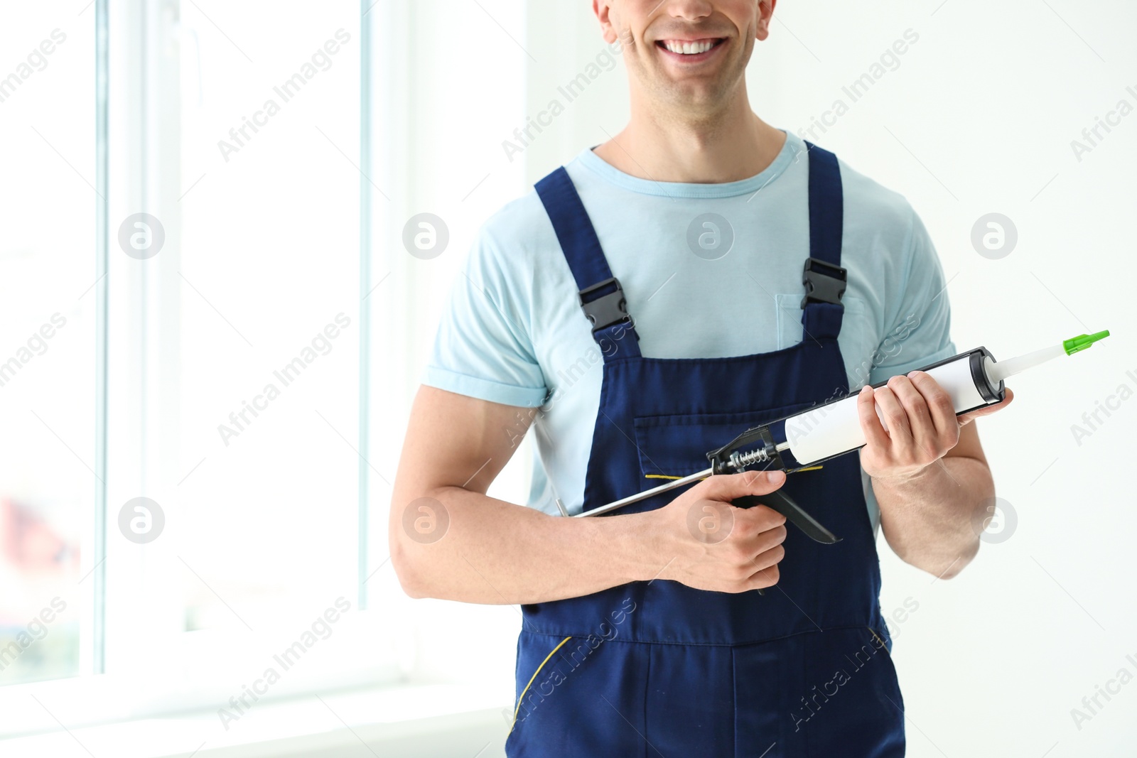 Photo of Construction worker in uniform with window sealant indoors