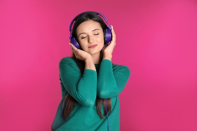 Attractive young woman enjoying music in headphones on color background