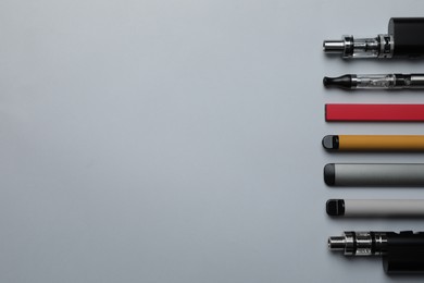 Photo of Many different electronic cigarettes on light background, flat lay. Space for text