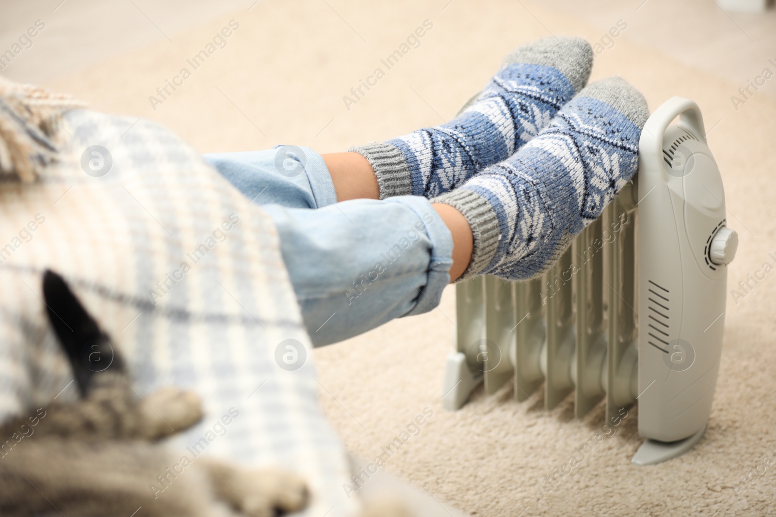 Photo of Woman warming feet on electric heater at home, closeup