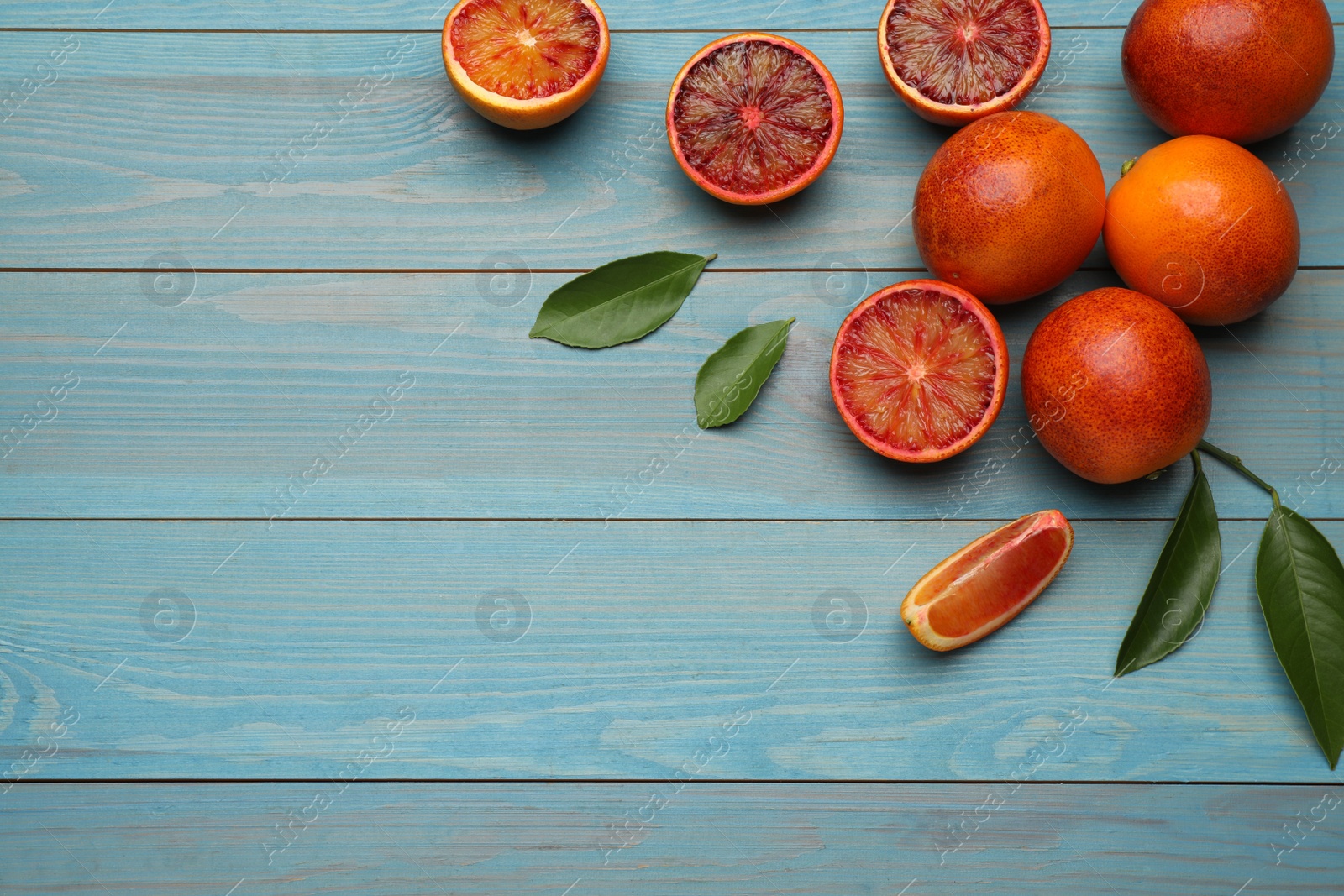 Photo of Many ripe sicilian oranges and leaves on light blue wooden table, flat lay. Space for text