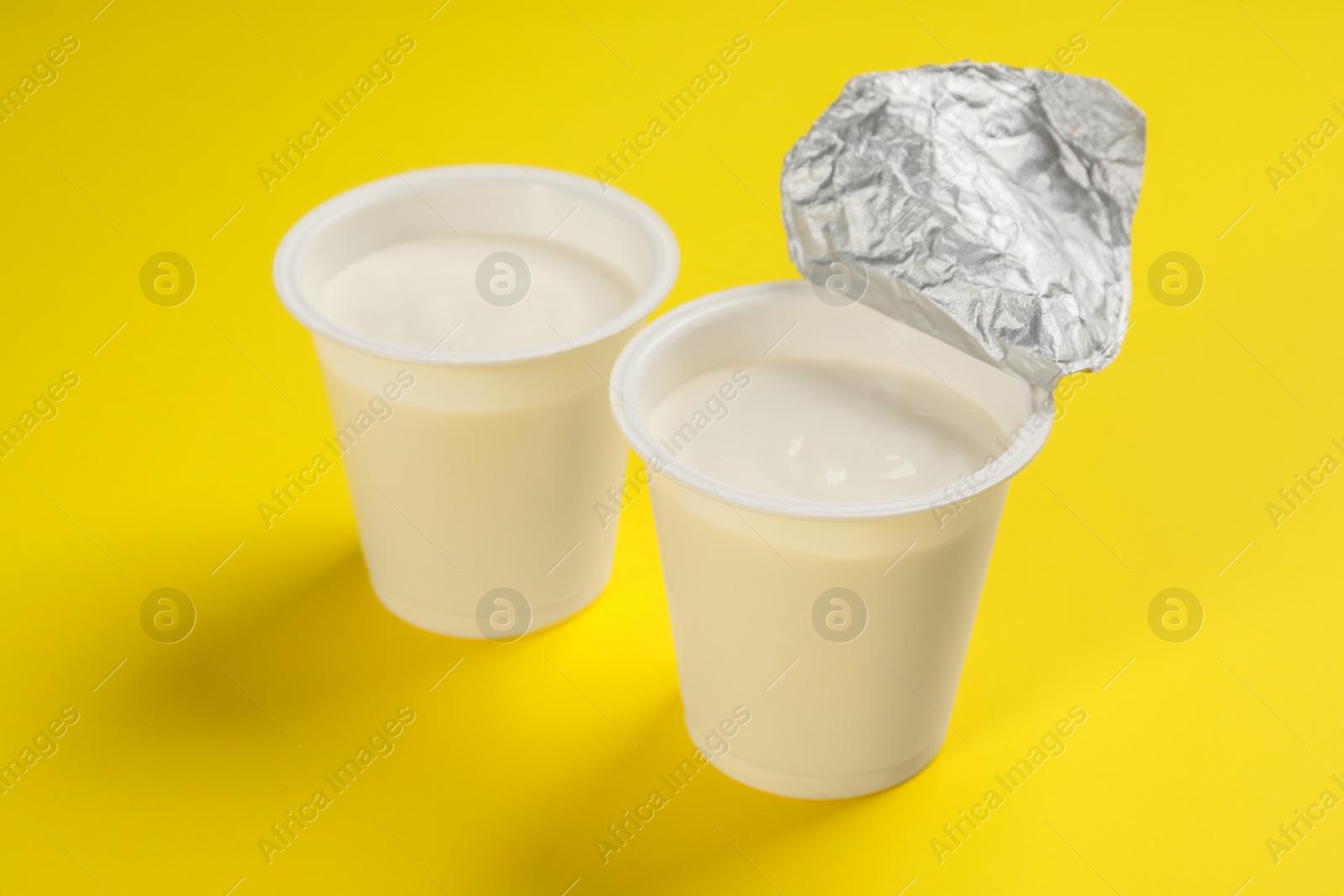 Photo of Plastic cups with tasty yogurt on yellow background