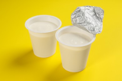 Photo of Plastic cups with tasty yogurt on yellow background