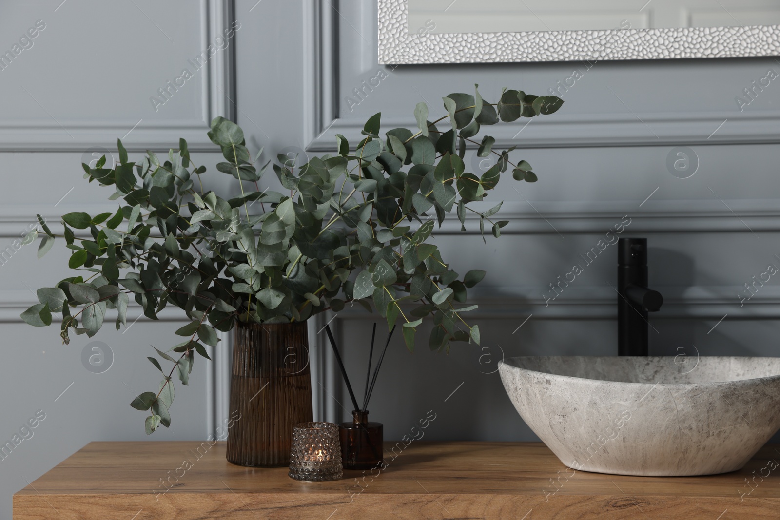 Photo of Eucalyptus branches, candle and aroma sticks near vessel sink on bathroom vanity. Interior design