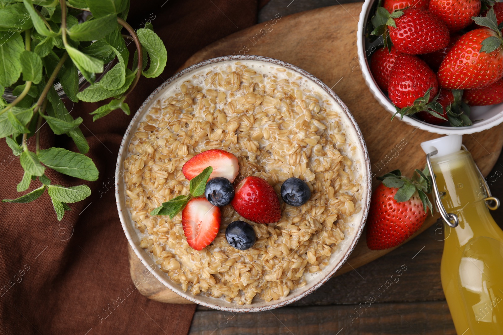 Photo of Tasty oatmeal with strawberries and blueberries in bowl on wooden table, flat lay