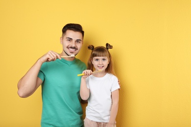 Photo of Little girl and her father brushing teeth together on color background, space for text