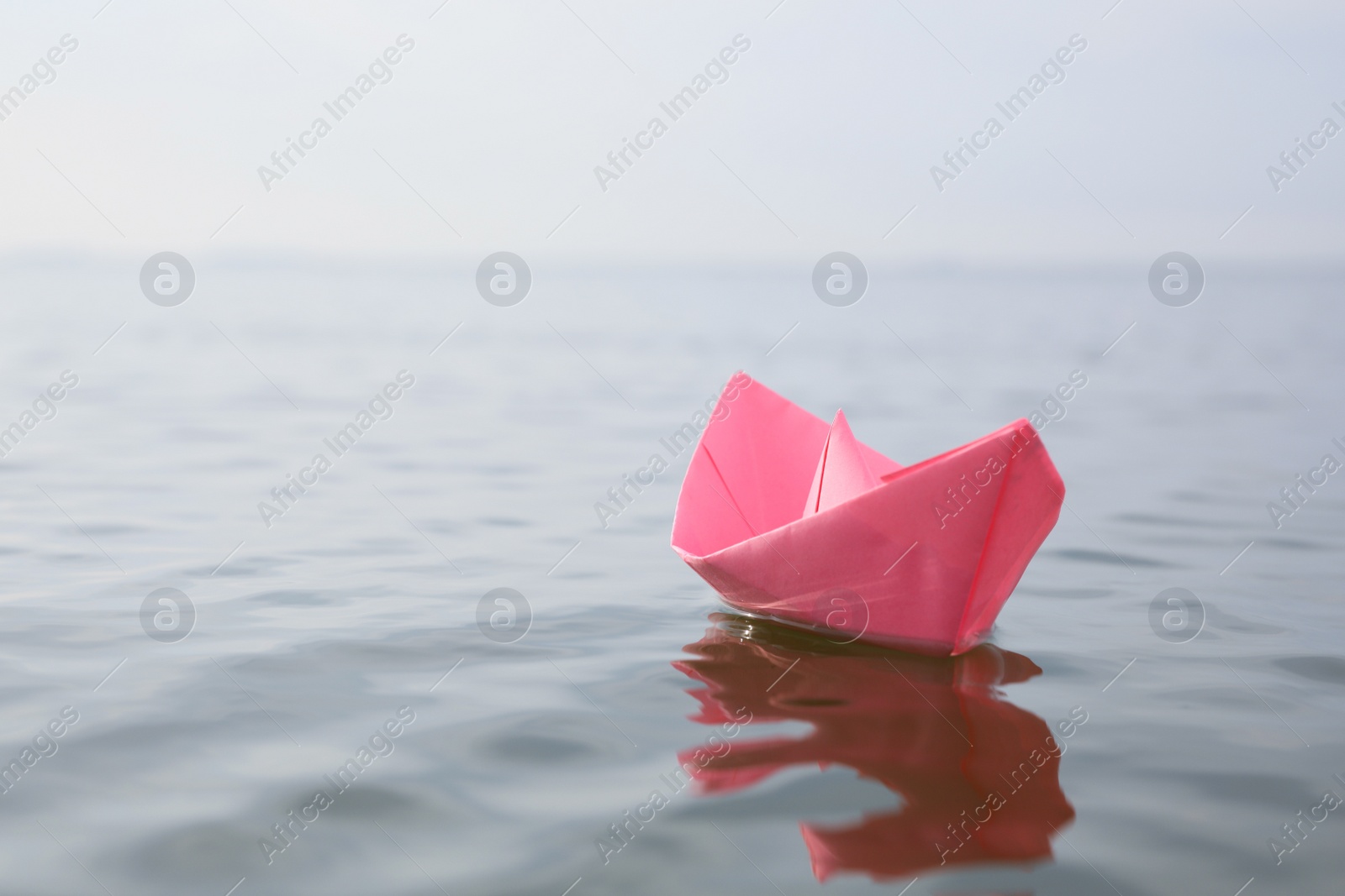 Photo of Pink paper boat on water surface, space for text