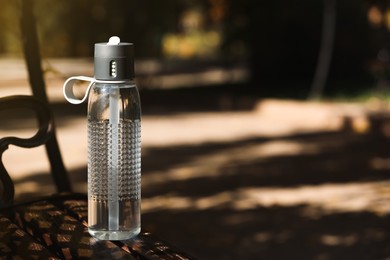 Photo of Sport bottle of water on wooden bench in park, space for text