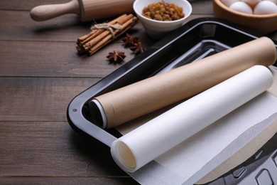 Photo of Rolls of parchment paper in baking pan and different ingredients on wooden table