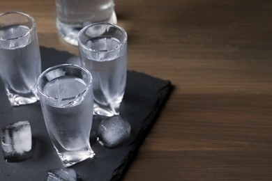 Photo of Shot glasses of vodka with ice cubes on wooden table. Space for text