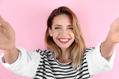 Beautiful laughing woman taking selfie on color background