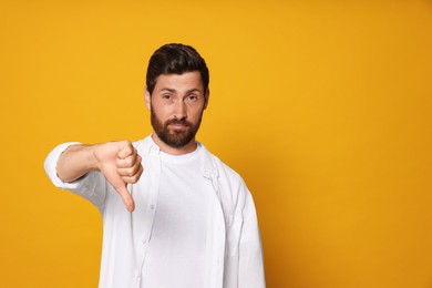 Photo of Handsome bearded man showing thumb down on orange background. Space for text