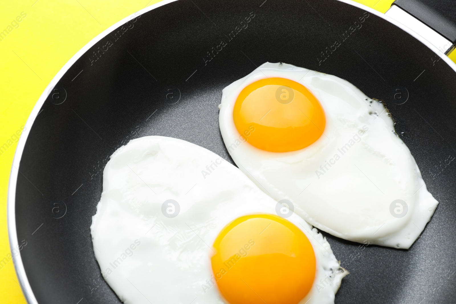 Photo of Tasty fried eggs in pan on yellow background, closeup