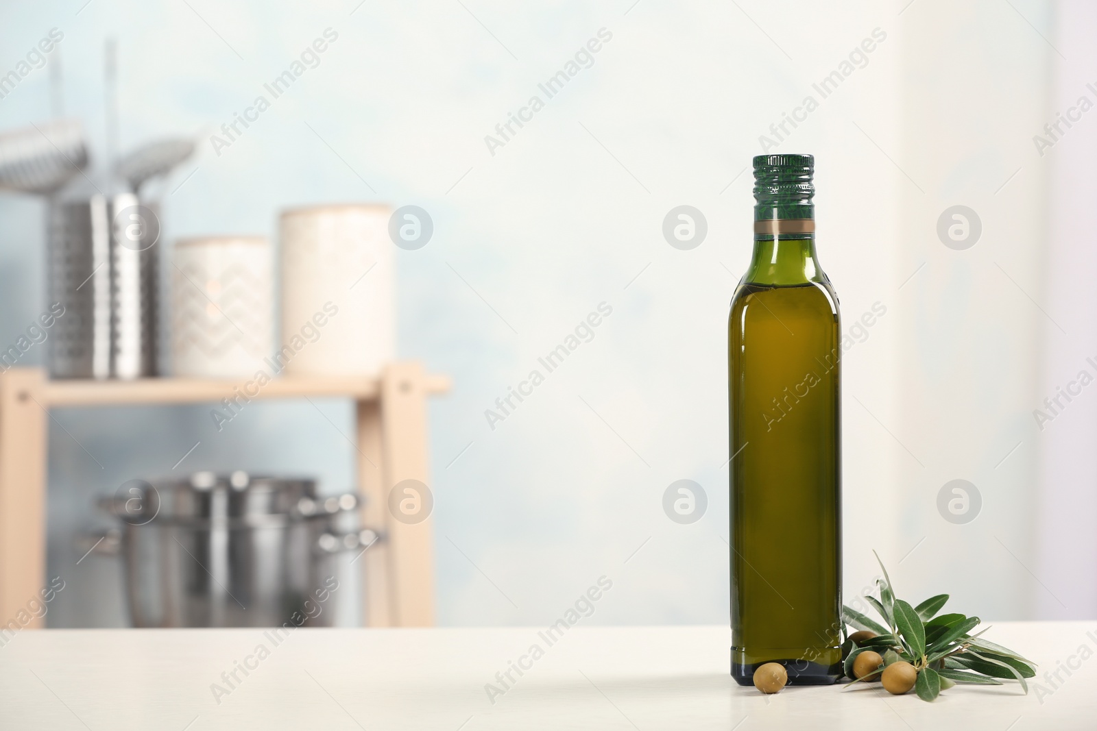 Photo of Bottle of oil and olive tree twig on table against blurred background. Space for text