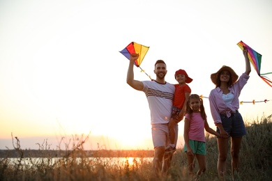 Photo of Happy parents and their children playing with kites outdoors at sunset. Spending time in nature