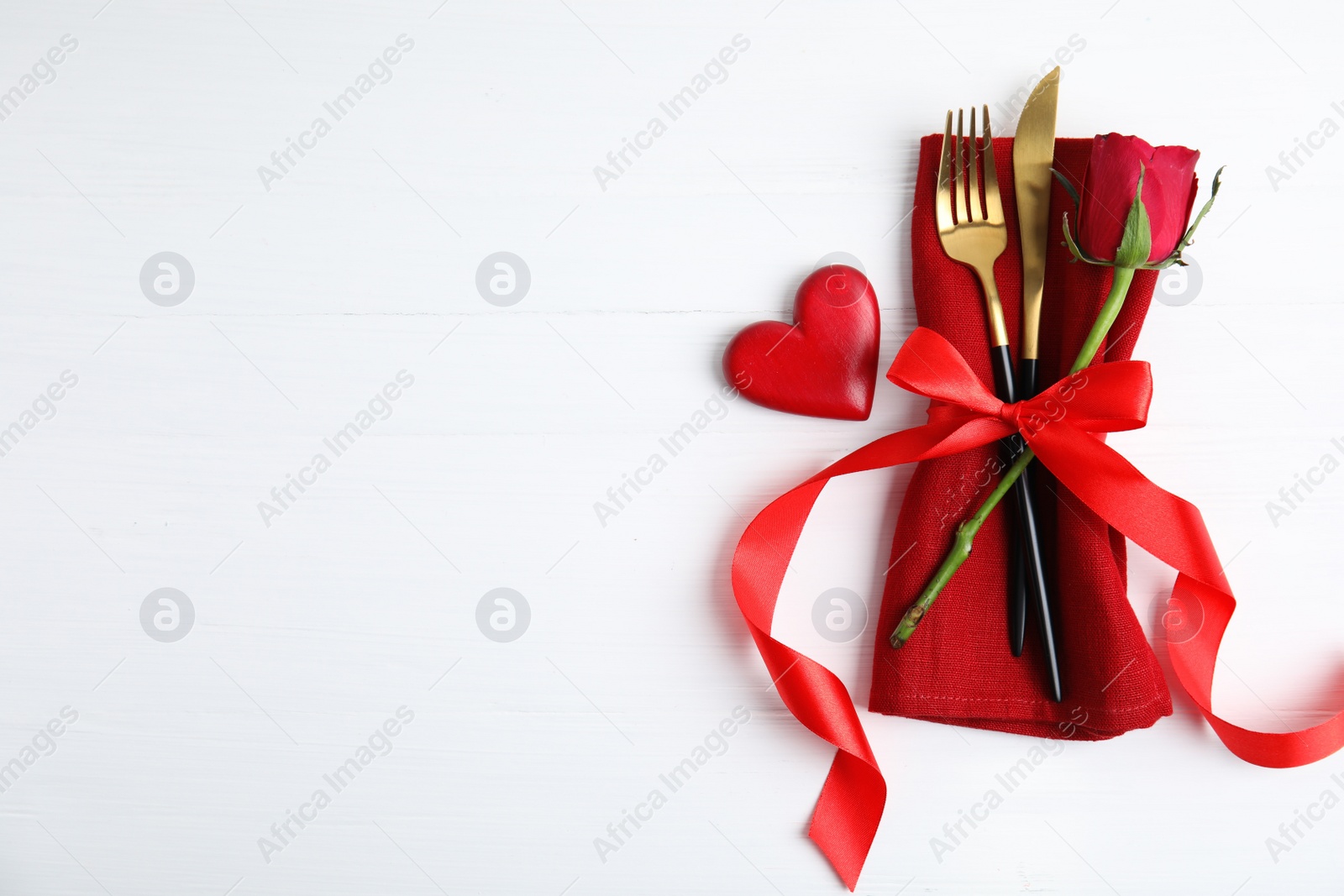 Photo of Top view of cutlery with napkin and decorative heart on white wooden table, space for text. Valentine's Day romantic dinner