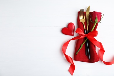 Top view of cutlery with napkin and decorative heart on white wooden table, space for text. Valentine's Day romantic dinner