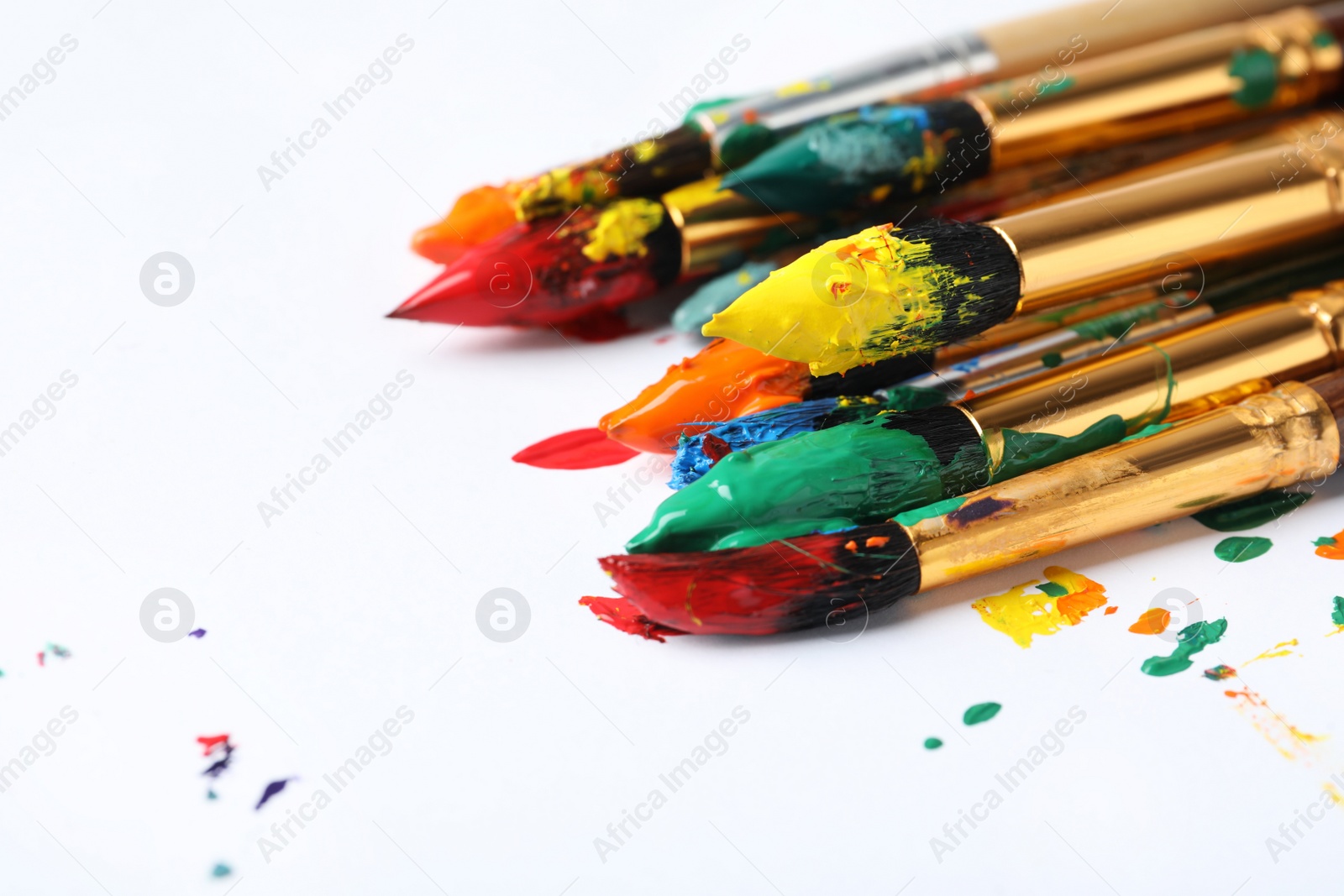 Photo of Brushes with colorful paints on white background, closeup. Space for text