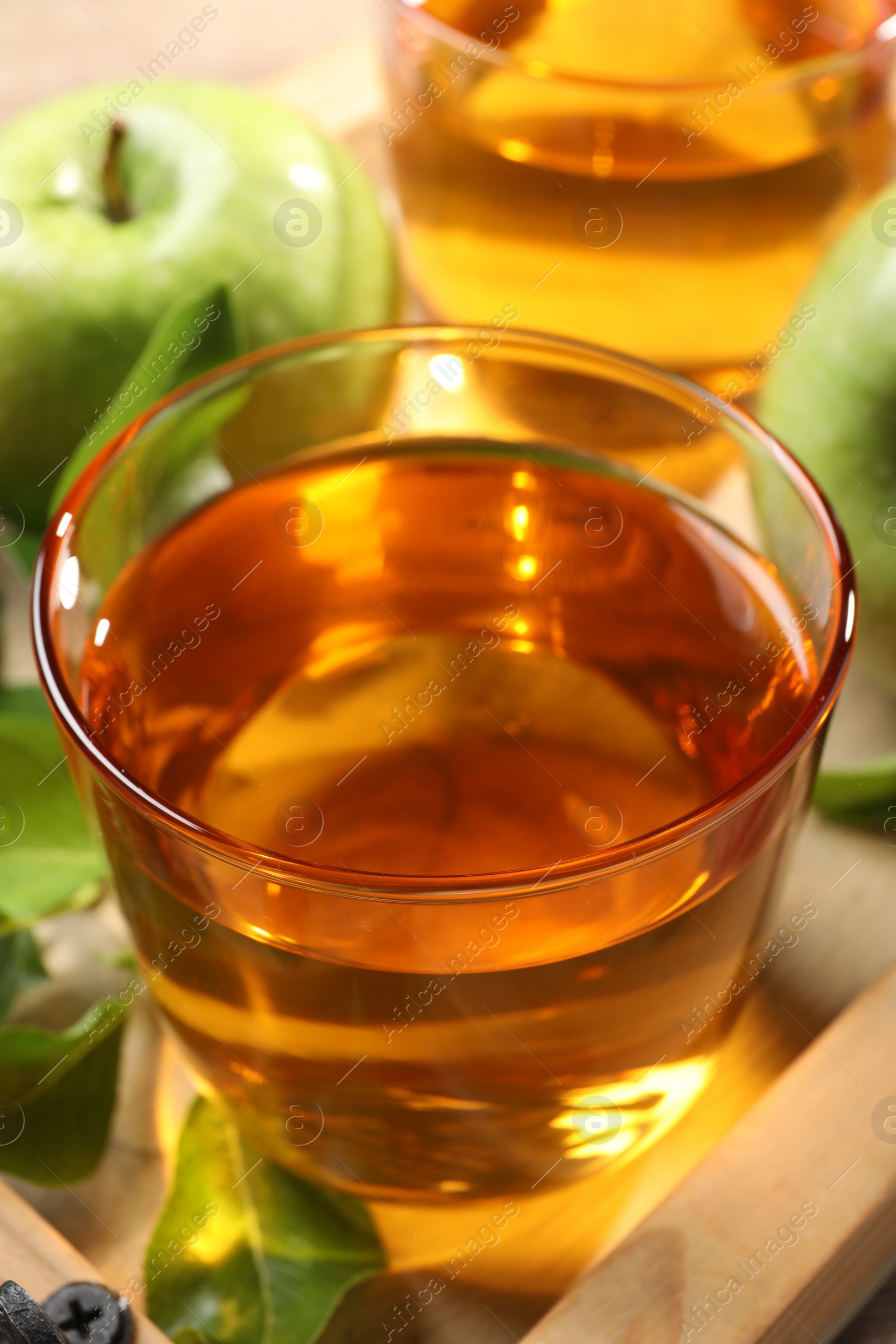 Photo of Glass of fresh apple juice on wooden tray, closeup