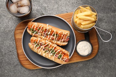 Delicious hot dogs with bacon, carrot and parsley served on grey table, flat lay
