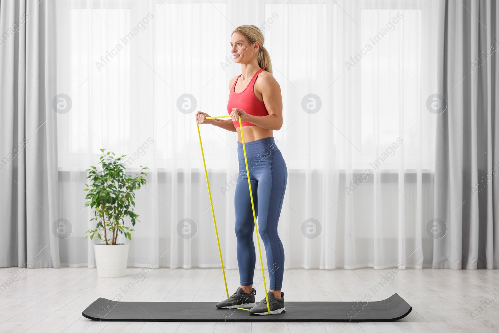 Photo of Athletic woman doing exercise with fitness elastic band on mat at home