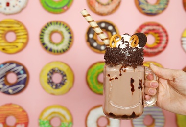 Woman holding mason jar of tasty milk shake with sweets near decorated wall, closeup. Space for text