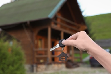 Photo of Real estate agent holding key and blurred house on background. Focus on hand