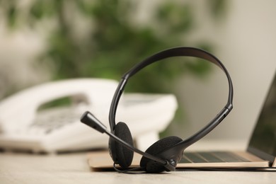 Photo of Headset, desktop telephone and laptop on table indoors, closeup. Hotline concept