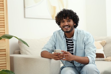 Photo of Handsome smiling man using smartphone in room, space for text