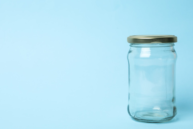 Closed empty glass jar on light blue background, space for text