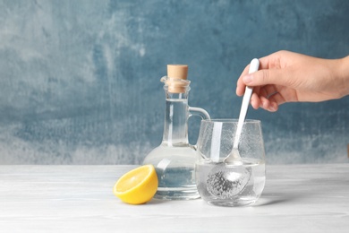 Photo of Woman mixing vinegar and baking soda in glass on table. Space for text