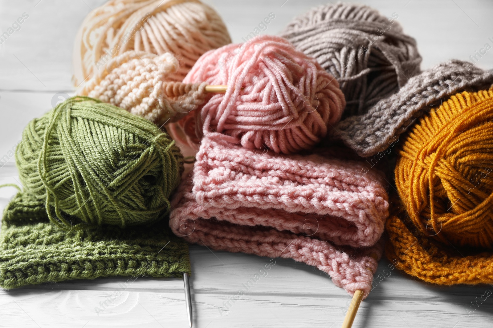 Photo of Balls of soft yarns, knitting and needles on white wooden table