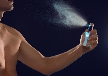 Young man spraying perfume on black background, closeup