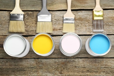 Photo of Cans of colorful paints with brushes on wooden table, flat lay