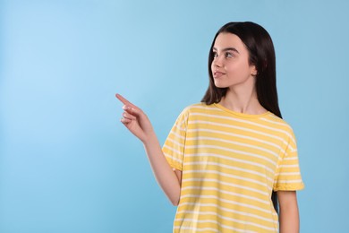 Teenage girl pointing at something on light blue background. Space for text